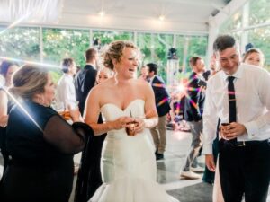 Bride and groom on dance floor, smiling in a crowd of their guests